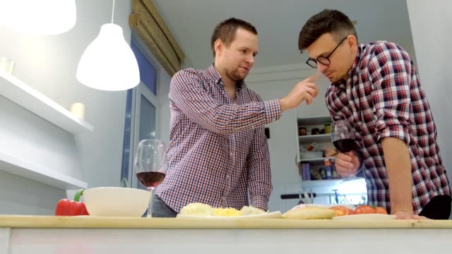 Un-par-de-hombres-gays-coquetan-entre-sí-cocinando-una-pizza-juntos-y-bebiendo-un-vino.
