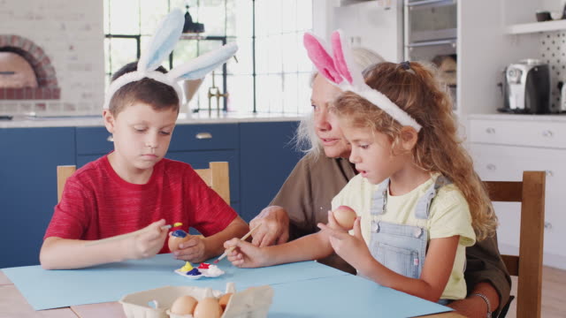 Abuela-con-nietos-vistiendo-orejas-de-conejo-decorar-huevos-de-Pascua-en-casa-juntos