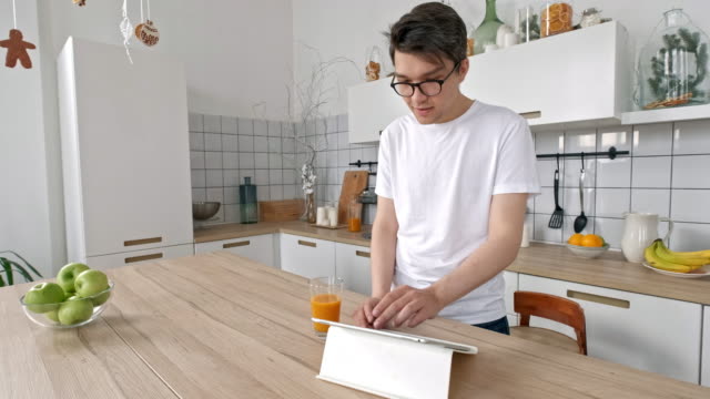 Attraktiver-Mann-zu-Hause-mit-Tablet-in-der-Küche-senden-Botschaft-auf-Social-Media-Lächeln-genießen-modernen-Lebensstil-trägt-weißes-Hemd