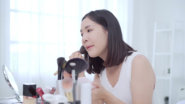 Beauty-Blogger-präsentieren-Beauty-Kosmetik-sitzen-vor-der-Kamera-für-die-Aufnahme-von-Video.-Glücklich-schöne-junge-asiatische-Frau-verwenden-Kosmetik-Rezension-Make-up-Tutorial-übertragen-Live-Video-an-soziale-Netzwerk.