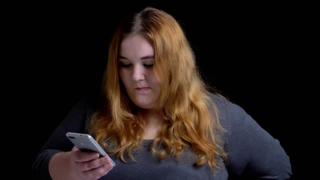 Closeup-shoot-of-young-overweight-caucasian-female-browsing-on-the-phone-and-reacting-top-social-media-posts-then-looking-at-camera-and-smiling