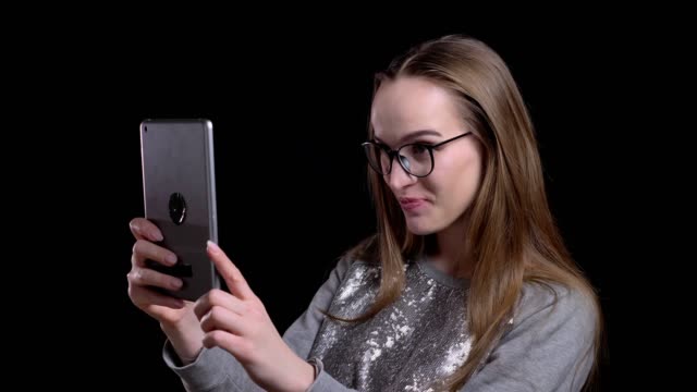 Closeup-shoot-of-young-attractive-hipster-female-in-glasses-having-a-video-call-the-tablet-with-background-isolated-on-black