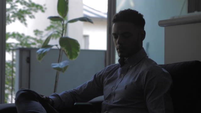 Young-afro-american-Businessman-taking-his-smartphone-in-his-living-room.-Social-network-account-feed,-news.-Medium-Shot.-Communication,-social-networking,-online-shopping,-chat-concept.
