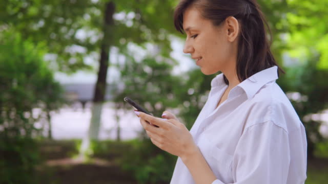 Junge-weibliche-Brünette-zu-Fuß-im-Park-und-SMS