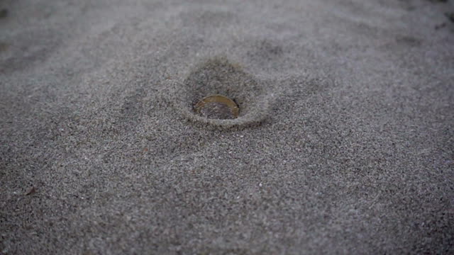 Slow-motion-euro-coins-fall-and-burrow-into-a-pile-of-sand.