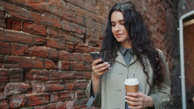 Glückliche-Frau-mit-Smartphone-berühren-Bildschirm-und-lächelnd-gehen-im-Freien