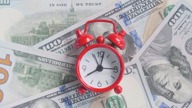 Red-alarm-clock-walking-ticking-on-the-background-of-American-hundreds-dollar-bills,-closeup.-Concept-Time-is-money,-Timelapse