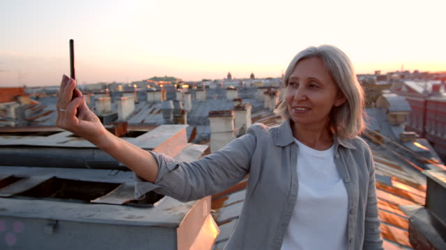 Grauhaarige-Frau-mittleren-Alters-macht-Selfie-auf-dem-Dach