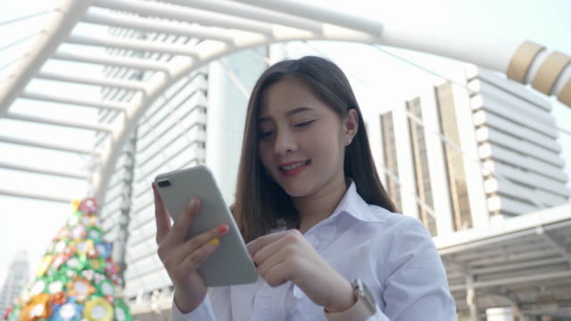 Young-smiling-business-asian-woman-using-smartphone-in-the-modern-city-center-in-the-evening-of-Bangkok-Thailand.-Concept-Technology-communication-by-mobile-phone