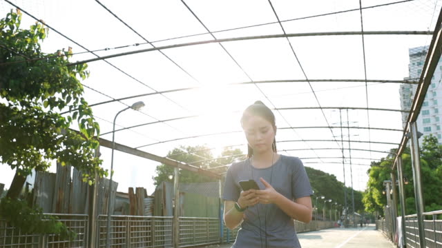 Hermosa-chica-asiática-atletas-caminando-usando-teléfonos-inteligentes-escribiendo-mensaje-de-medios-sociales-después-de-correr.-Jogging-estilo-de-vida-de-entrenamiento-en-la-calle-al-atardecer.