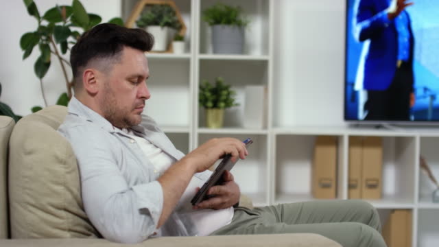 Mittlerer-Alter-Mann-Fernsehen-und-Mit-Tablet-zu-Hause