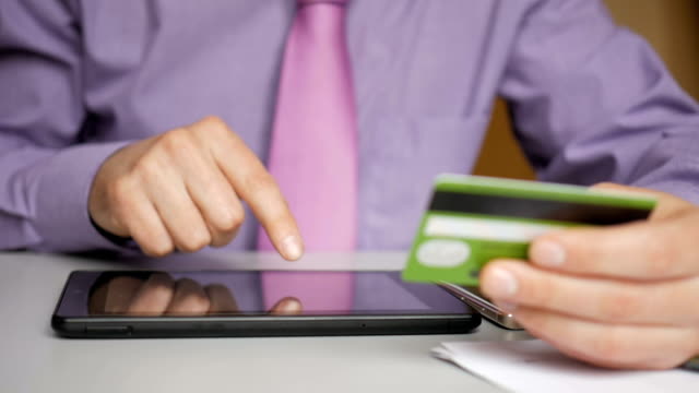 Ein-Geschäftsmann-in-einem-lila-Hemd-und-Krawatte-macht-eine-Zahlung-an-Internet-Banking.-Online-Shopping-mit-Kreditkarte-auf-digitalem-Tablet.