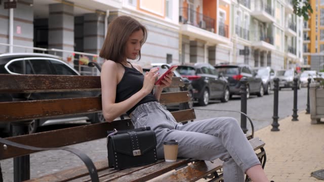 Chica-linda-utilizar-teléfono-inteligente-rojo-al-aire-libre