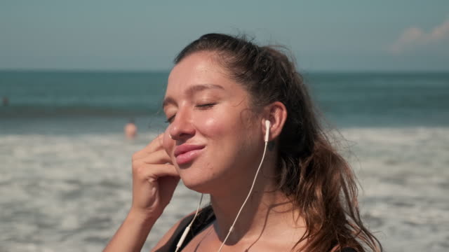 Sportswoman-listening-to-the-music-at-sandy-coastline-of-ocean
