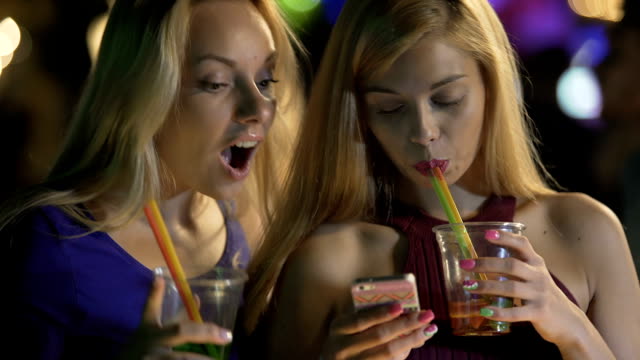 Pretty-girls-drinking-cocktails-at-bar,-checking-social-networks-on-smartphone