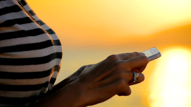 Close-up-Frau-die-Hände-mit-Smartphone-in-eine-Reise-durch-das-Meer-auf-den-Sonnenuntergang.