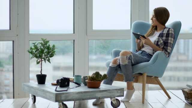 Attraktive-Frau-mit-digital-Tablette-sitzen-im-Stuhl-auf-Balkon-im-modernen-Loft-Wohnung