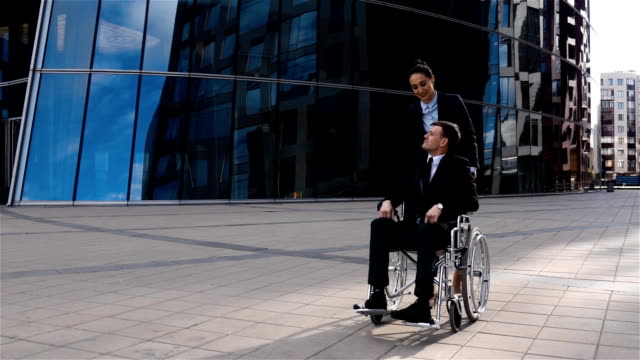 Hübsche-Geschäftsfrau-kümmert-sich-um-seine-Kollegin-im-Rollstuhl