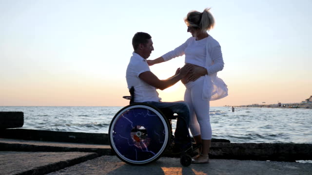 behinderte-Mensch-streichelt-Frau-mit-großen-Bauch-am-Ufer,-Behinderten-im-Rollstuhl-hört-Bauch