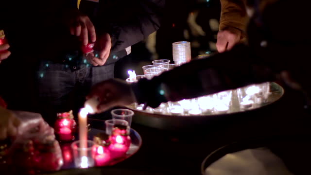 Group-of-people-lighting-dozens-of-candles-in-plastic-glasses,-light-at-night