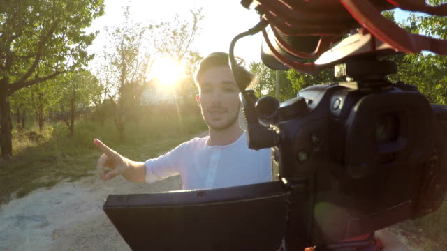 Begeistert-jungen-Mann-dreht-und-eine-Videoaufnahme-außerhalb-seines-Hauses-mit-einer-mobilen-professionellen-Kamera-über-sein-Dorf-in-der-Natur