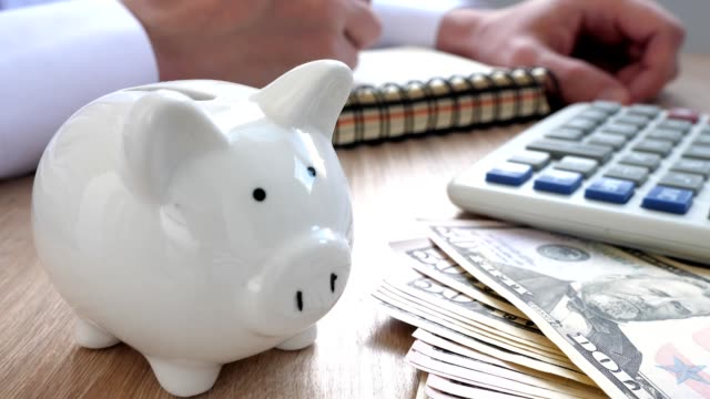 Savings-concept.-Piggy-bank,-calculator-and-man-writing-budget-in-a-note.