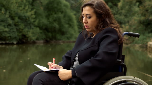 mujer-en-silla-de-ruedas-escribe-una-carta-de-amor-junto-al-lago
