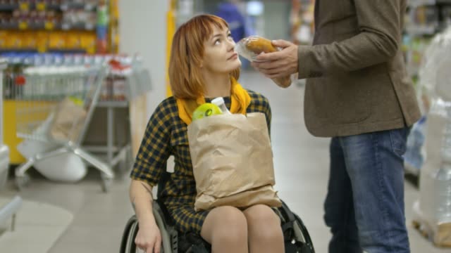 Mujer-con-discapacidad-en-silla-de-ruedas-de-compras-en-el-mercado-de-comestibles-con-su-novio