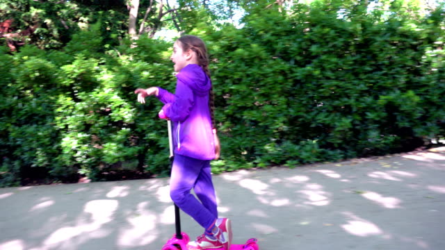 Little-child-learning-to-ride-a-scooter-in-a-city-park