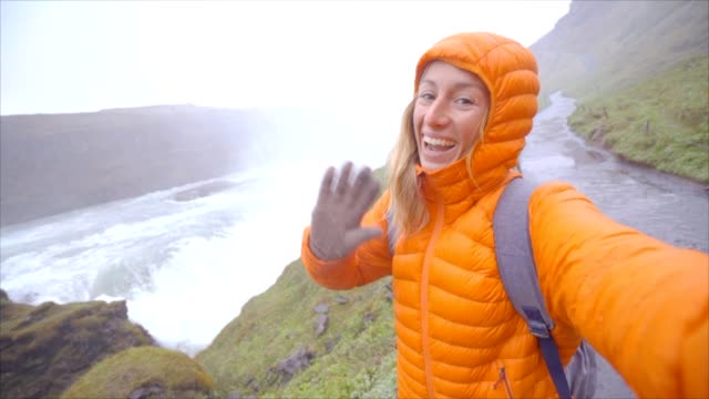 CÁMARA-lenta-Selfie-retrato-de-mujer-joven-junto-a-la-gran-cascada,-Islandia
