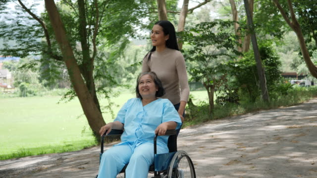 Mujer-mayor-con-su-hija-empujando-la-silla-de-ruedas-por-el-Parque