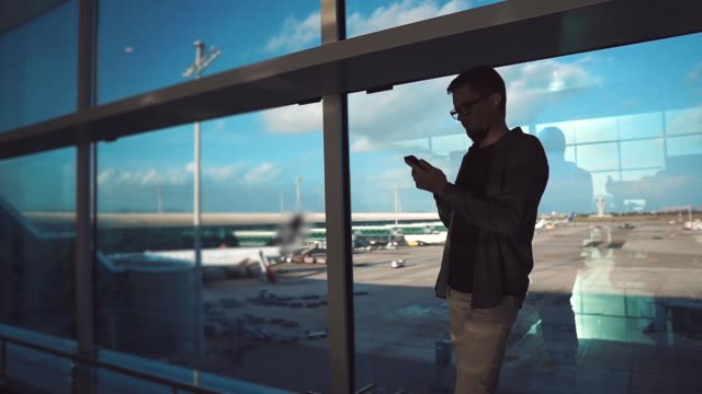 Male-traveler-is-reading-news-tape-in-social-networks-by-smartphone-in-airport