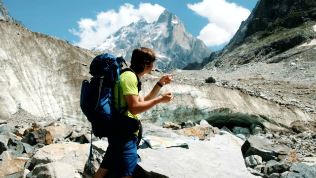 Tourist-man-with-a-backpack-exploring-the-route-on-the-map-and-phone-GPS,-adds-a-map-and-goes-on-a-route-in-the-mountain-hike