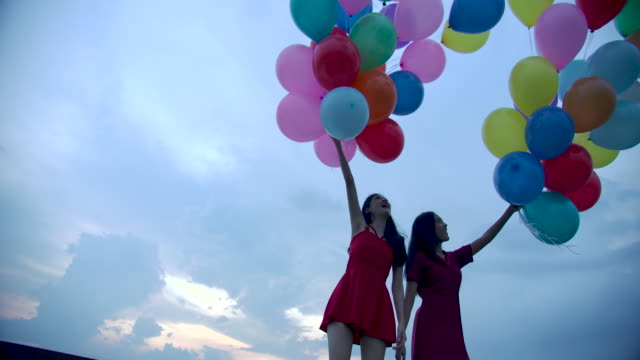 Two-girls-holding-balloon-with-sky-background-in-slow-motion.