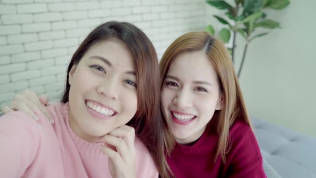 Asian-blogger-women-using-smartphone-selfie-and-recording-vlog-video-in-living-room-at-home,-group-of-friend-enjoy-funny-moment-while-lying-on-the-sofa-when-relax-at-home.-Point-of-view.