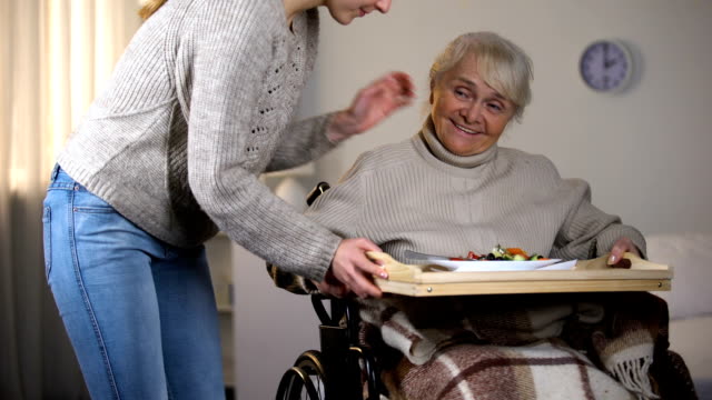 Female-volunteer-serving-dinner-to-handicapped-old-women,-elderly-sitter-service