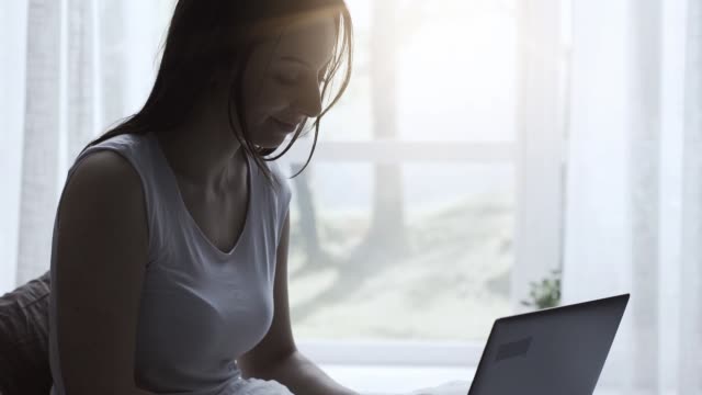 Woman-lying-in-bed-and-connecting-with-her-laptop