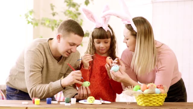 familia-con-hija-decoran-los-huevos-de-Pascua-y-miran-a-la-hija.