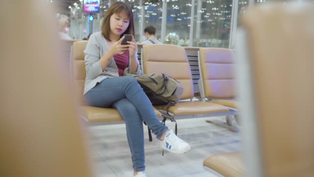 Asiatische-Frau-mit-Smartphone,-während-sie-auf-dem-internationalen-Flughafen-sitzt.