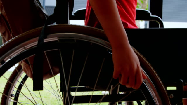 Vista-lateral-del-niño-de-escuela-afroamericano-con-discapacidades-moviendo-su-silla-de-ruedas-en-el-corredor-escolar-4k