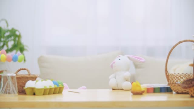 Joven-chica-adorable-se-esconde-bajo-la-mesa-llena-de-decoraciones-de-Pascua-y-está-jugando-con-el-conejo-de-Pascua-en-la-mano.