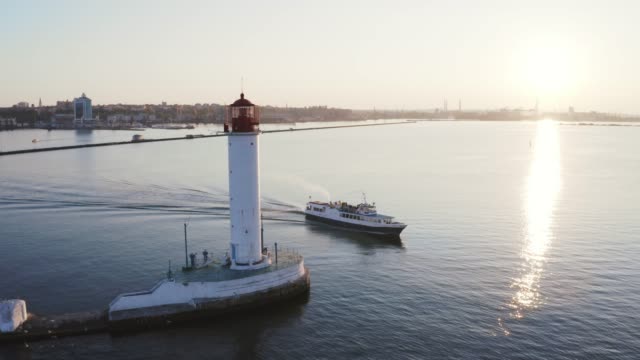 Luftaufnahme-von-weißem-Leuchtturm-in-der-Nähe-des-Seehafens,-während-Vergnügungsboot-vorbeikommt,-Drohne-gehen-360-aroung-Leuchtturm