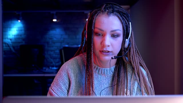 Closeup-shoot-of-young-attractive-female-blogger-with-dreadlocks-in-headphones-playing-video-games-and-streaming-live-with-the-neon-background