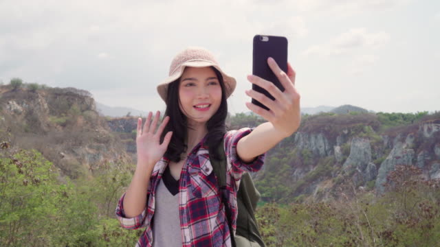 Blogger-Asian-backpacker-woman-record-vlog-video-on-top-of-mountain,-young-female-happy-using-mobile-phone-make-vlog-video-enjoy-holidays-on-hiking-adventure.-Lifestyle-women-travel-and-relax-concept.