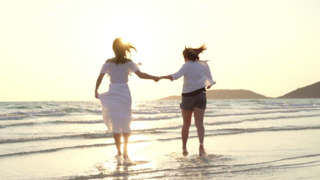 Young-Asian-lesbian-couple-running-on-beach.-Beautiful-women-friends-happy-relax-having-fun-on-beach-near-sea-when-sunset-in-evening.-Lifestyle-lesbian-couple-travel-on-beach-concept.