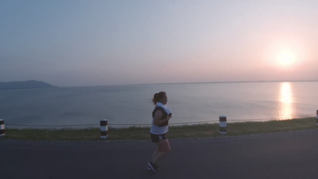 Asiatische-Frauen-joggen-in-der-Straße-am-frühen-Morgen-Sonnenlicht-am-Wasserspeicher-Pa-Sak-Jolasid-Dam.-Konzept-des-Gewichtsverlustes-mit-Bewegung-für-die-Gesundheit.-zeitlupe
