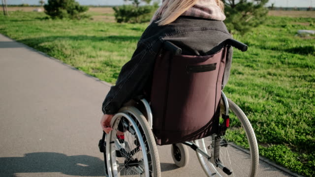 La-mujer-está-usando-silla-de-ruedas-para-moverse-al-aire-libre-en-un-día-soleado,-vista-trasera