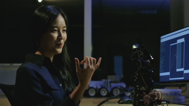 Jóvenes-ingenieros-de-desarrollo-de-electrónica-probando-tecnología-robótica-innovadora-en-laboratorio.-La-joven-hembra-asiática-crea-movimiento-para-la-mano-robótica-mecánica.-Personas-con-concepto-de-tecnología-o-innovación.