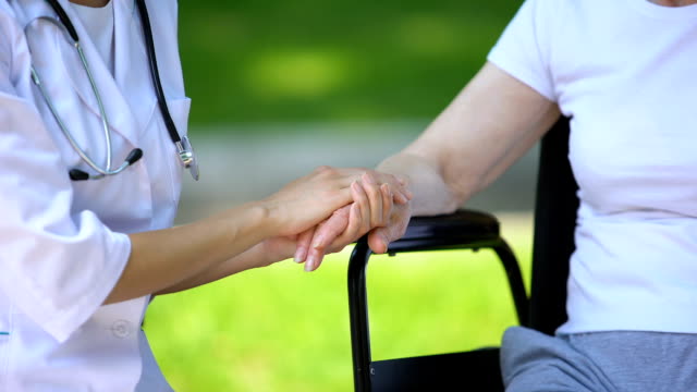 Terapeuta-femenina-sosteniendo-a-una-anciana-discapacitada-en-silla-de-ruedas,-al-aire-libre