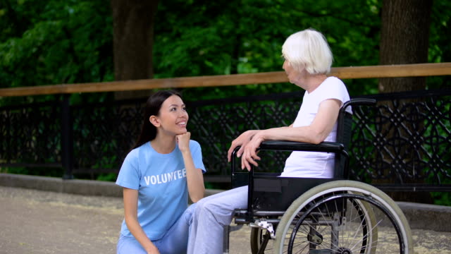 Glückliche-freiwillige-Zuhörer-in-den-Rollstuhl-sitzender-Seniorin,-Altenpflege